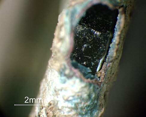 Mikroskopischer Blick in den Aufbau des Glasanhängers aus korrodiertem Messingrahmen, Papier und Glas